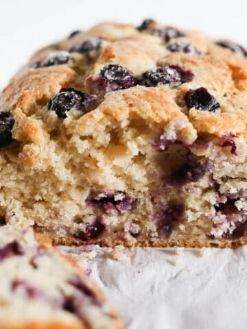 Blueberry bread loaf on the table with a slice cut so you can see the inside of the cake.