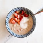 Strawberries and cream oatmeal in a blue designed bowl with a spoon and topped with fresh strawberries and yogurt.