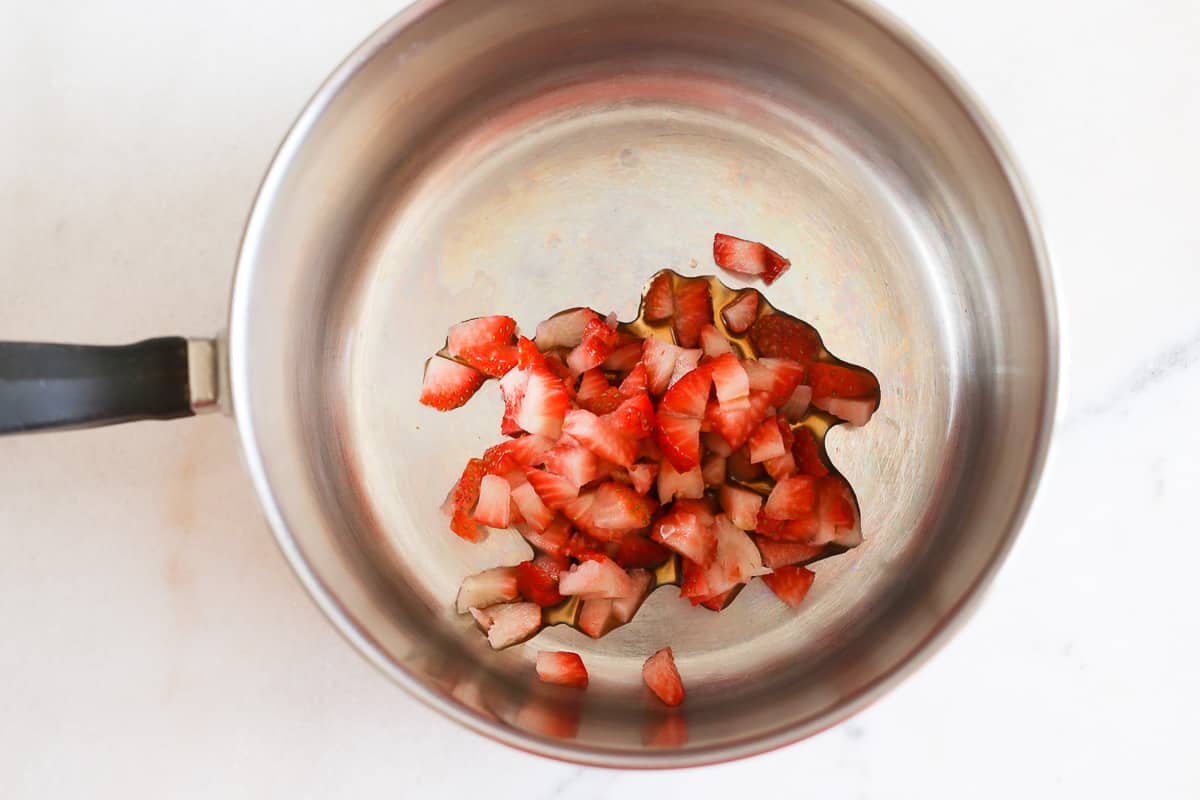 A silver cooking pot with tiny chopped fresh strawberry pieces and maple syrup ready to simmer.