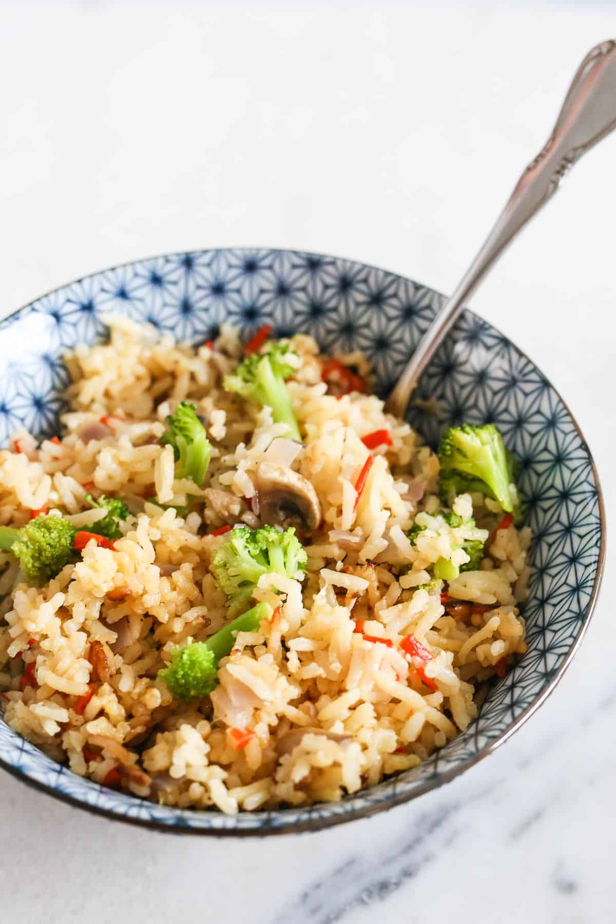 Rice and veggies in a blue and white bowl with a spoon on a marble table.