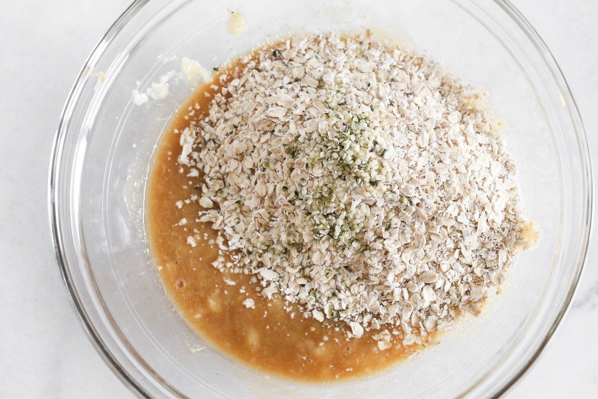 Broken up oat flour added to wet ingredients in a glass bowl.