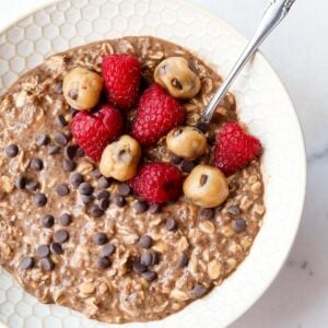 1200 x 1200 image of Chocolate Overnight Oats in a bowl topped with chocolate chips, edible cookie dough and raspberries.