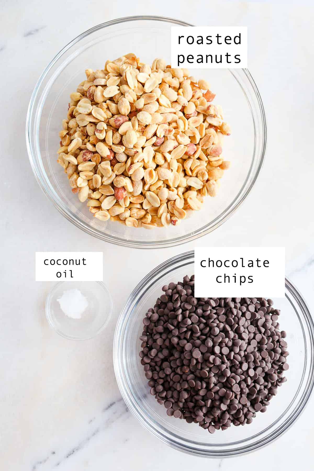 Ingredients to make Chocolate Peanut Clusters in small glass bowls sitting on a marble table,