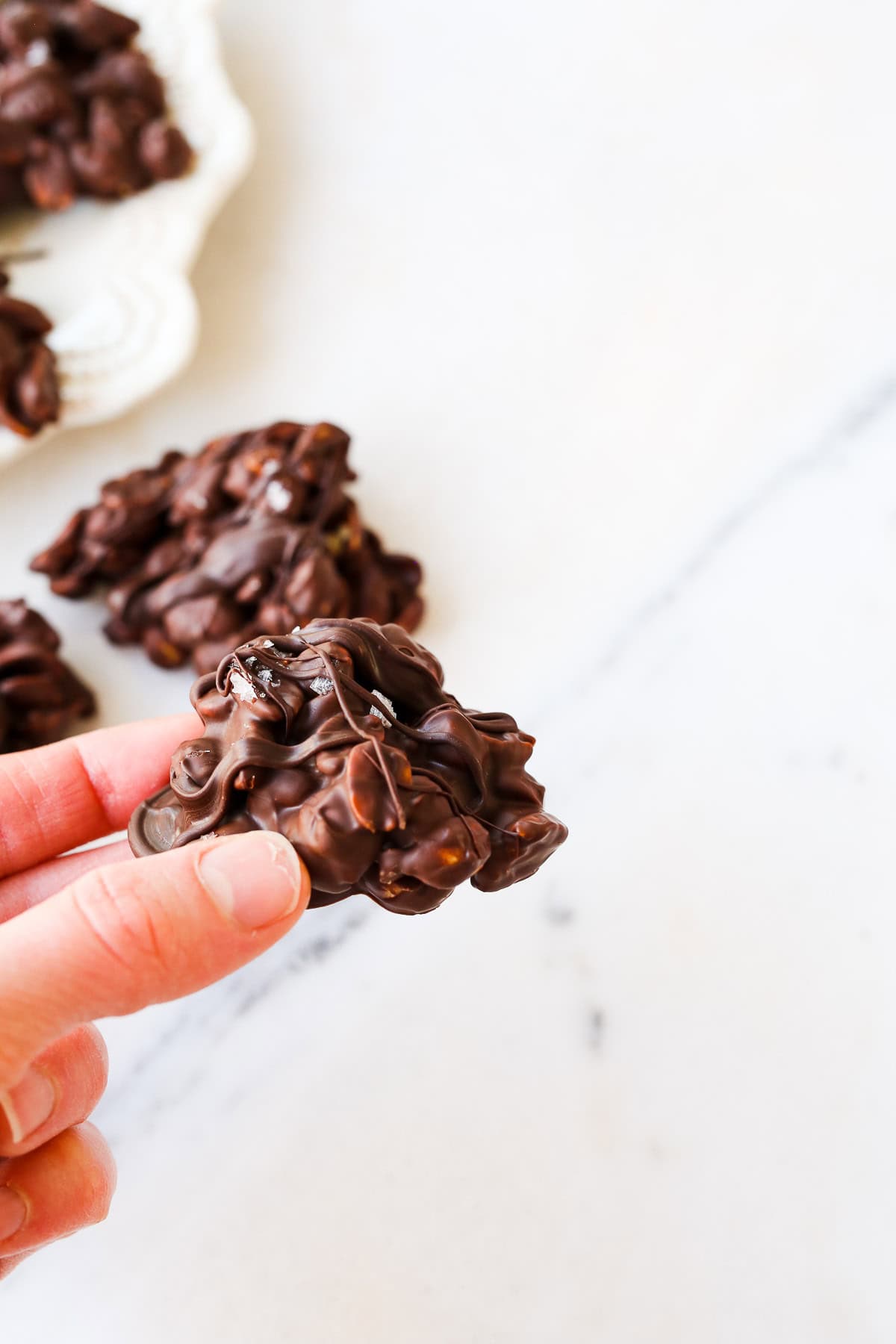 Chocolate Peanut Cluster being held in hand for picture.