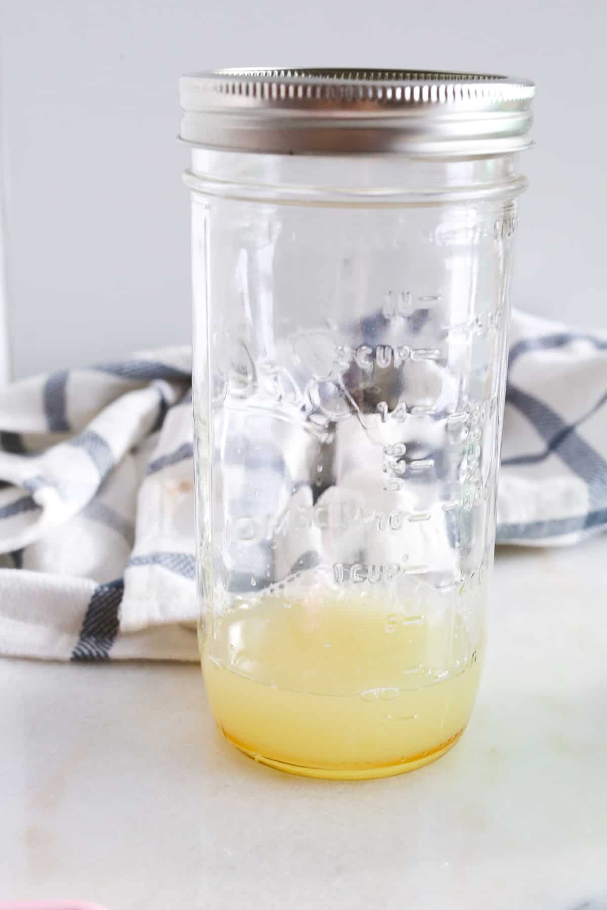 Glass jar with the lemon, lime and maple syrup added to it.