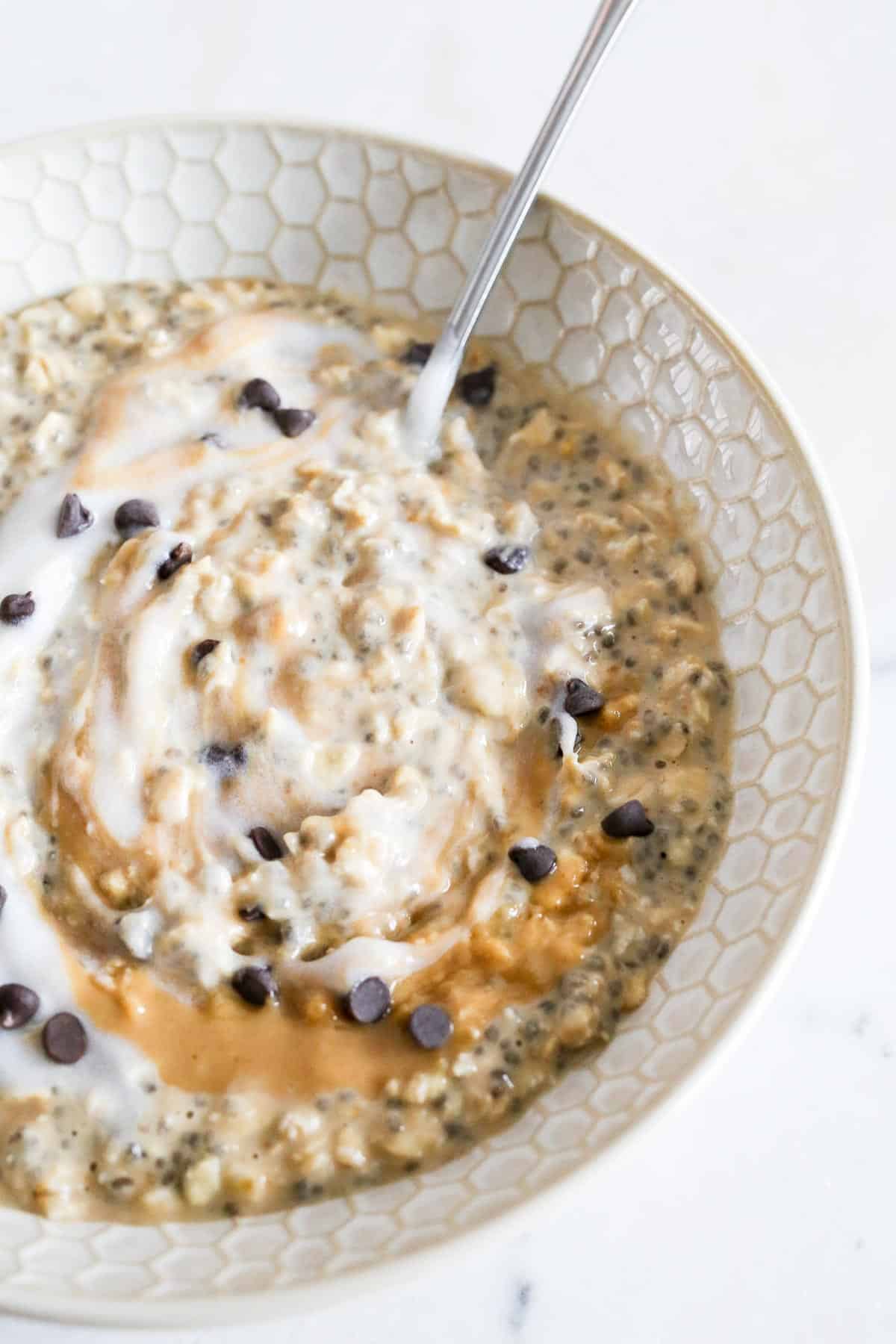 Peanut Butter Overnight Oats in a bowl topped with yogurt and peanut butter swirled in and mini chocolate chips.