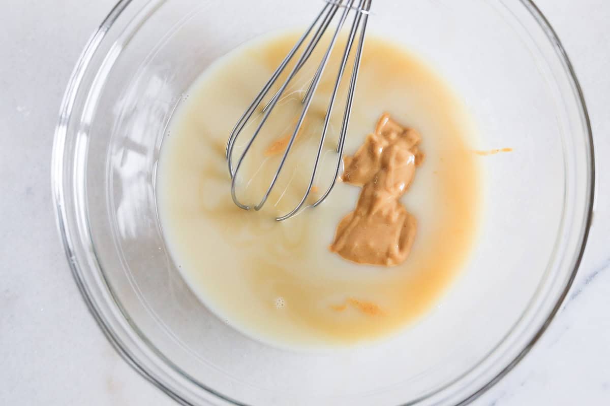 Milk, peanut butter, vanilla and maple syrup added to a glass bowl with a whisk.