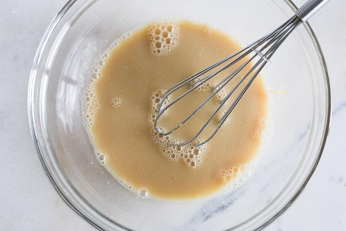 Milk, peanut butter, vanilla and maple syrup added to a glass bowl with a whisk and mixed well.