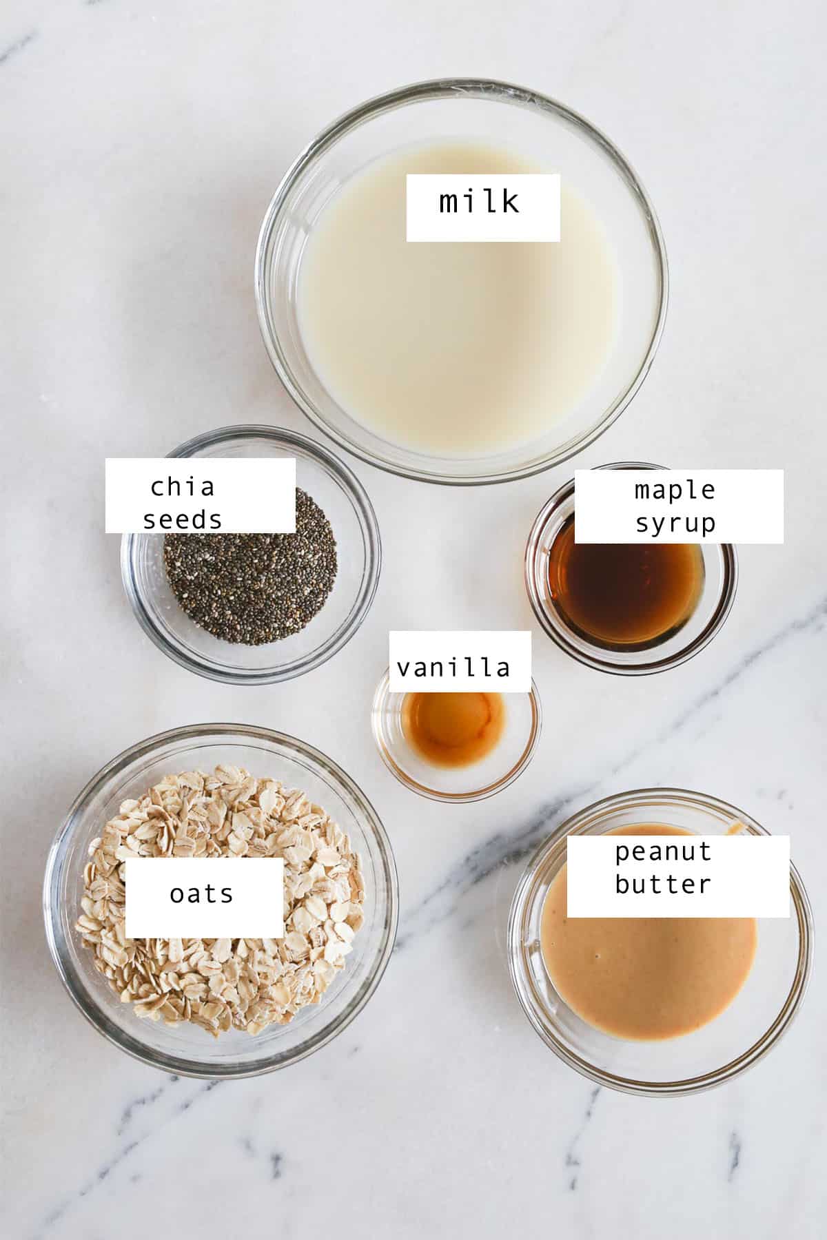 Ingredients to make peanut butter overnight oats in small glass bowls sitting on a marble table.