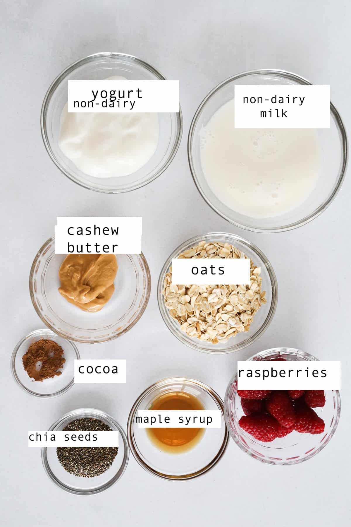 Small glass bowl of the ingredients to make raspberry overnight oats sitting on a marble table.