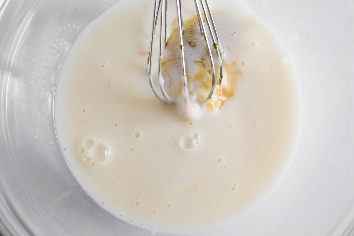 Clear glass bowl with the non-dairy milk and cashew butter with a whisk.