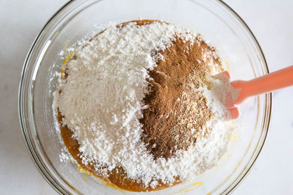 Flour added to wet ingredients in glass mixing bowl.