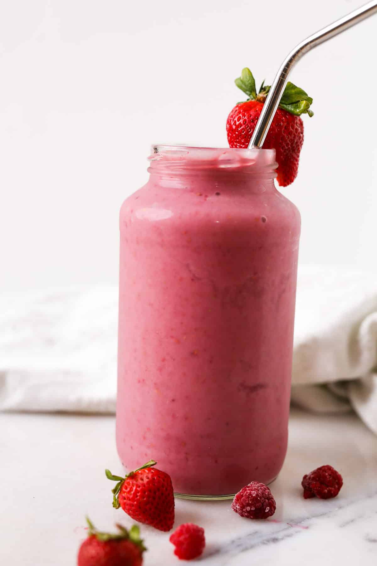 Strawberry Raspberry Smoothie side view close up with straw and strawberry garnish on top.