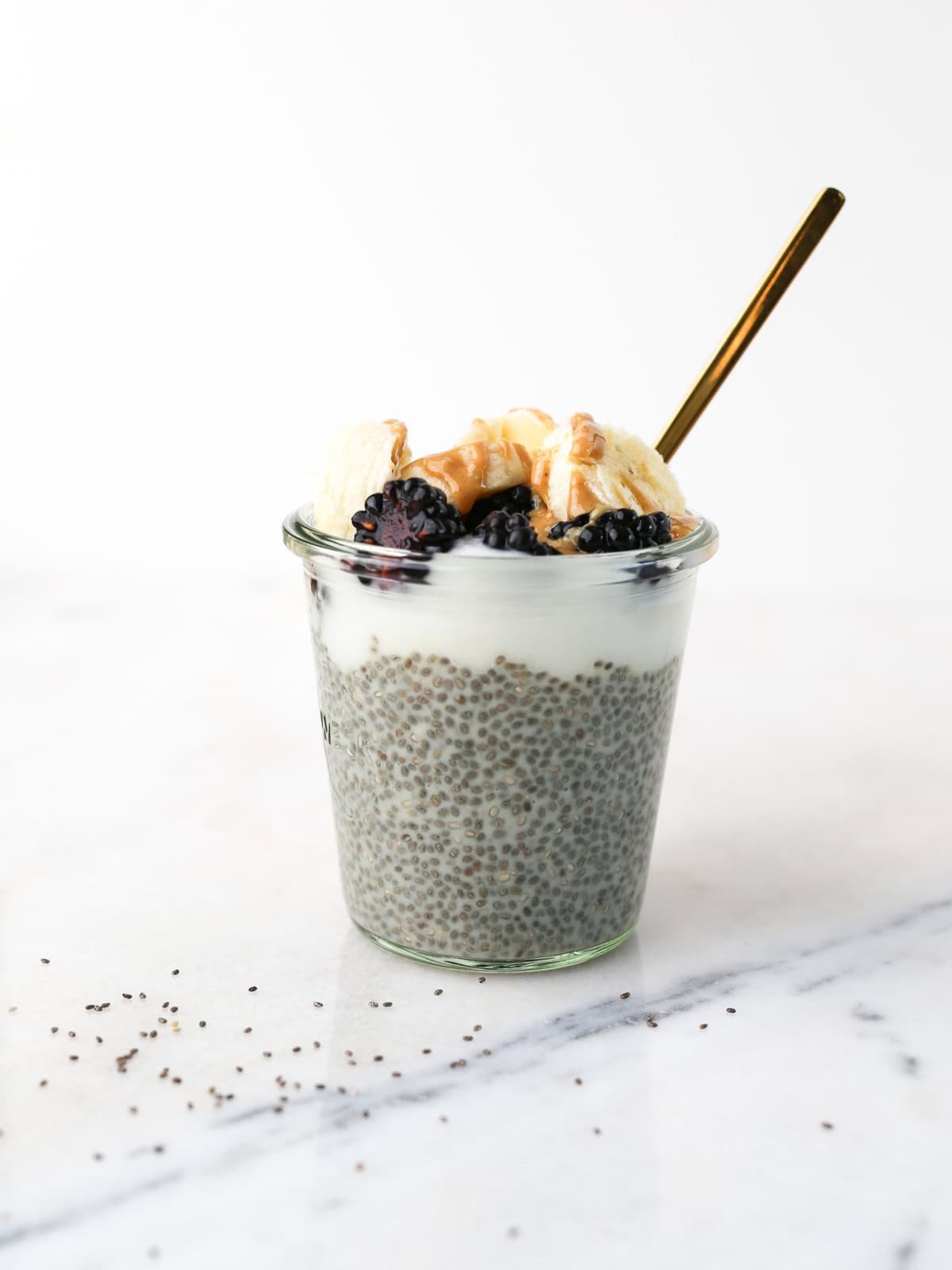 Chia seeds breakfast pudding in a glass jar topped with blackberries, yogurt, banana and peanut butter.