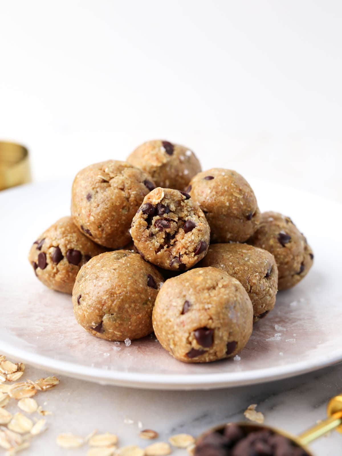 Chocolate peanut butter protein balls piled on top each other on a white plate with a bite taken out of one.