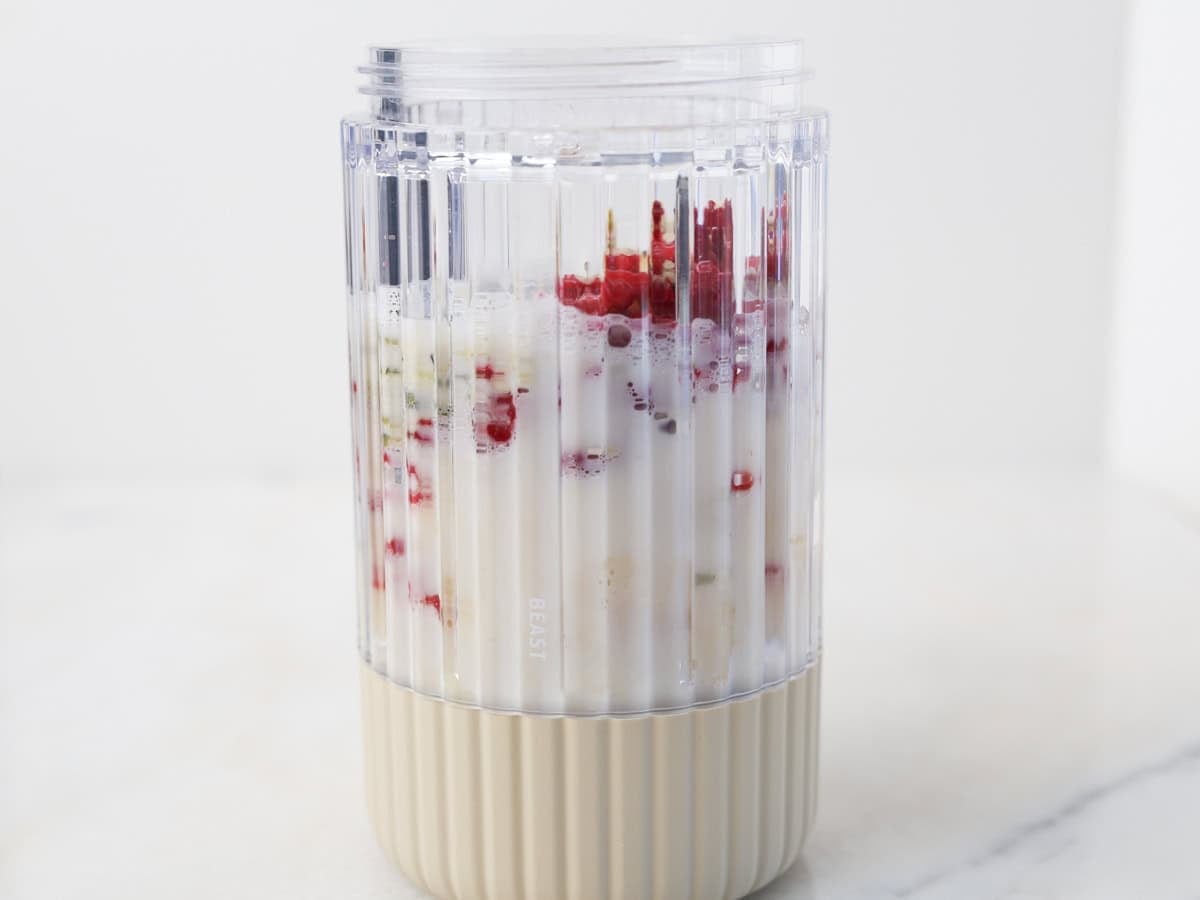 Blender with the ingredients to make this smoothie with mango and raspberry.