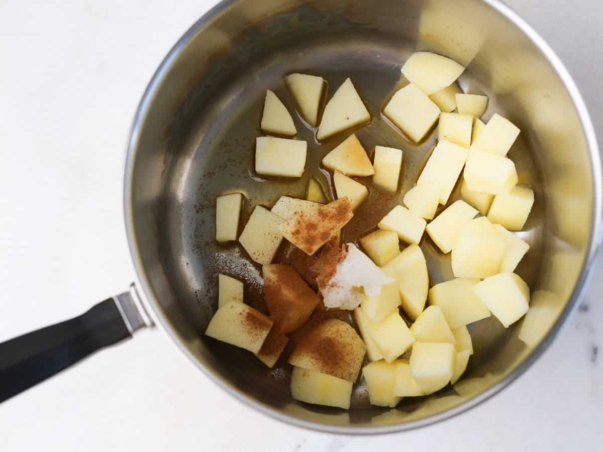 Pot with chopped apples, coconut oil, maple syrup and cinnamon.