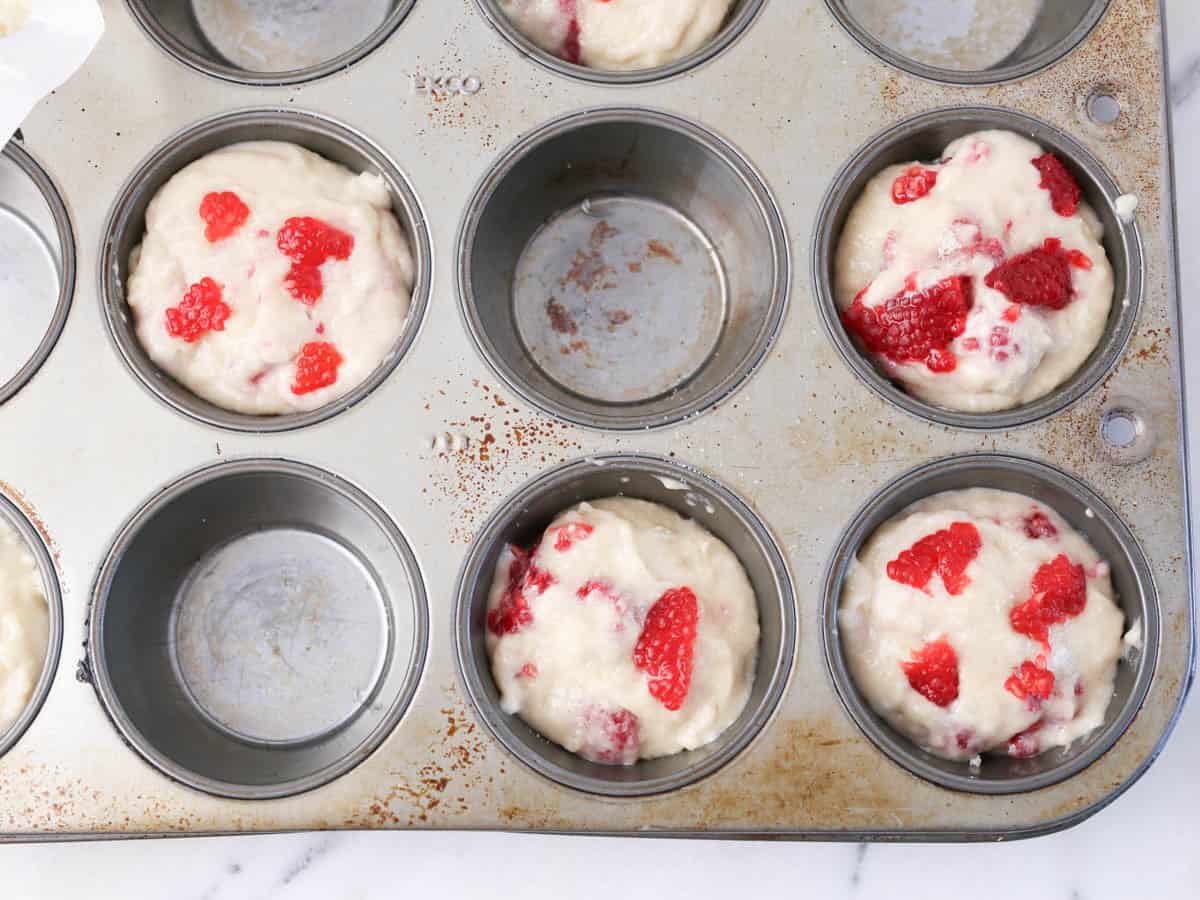 Muffin tin with batter added for vegan raspberry muffins.