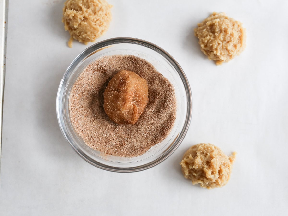 Snickerdoodle cookie dough being rolled in cinnamon sugar mixture.