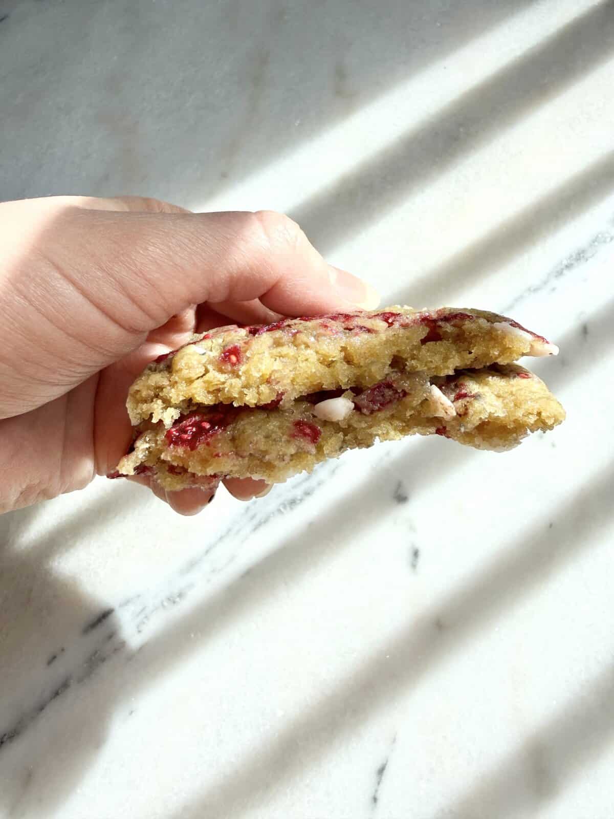 White chocolate raspberry cookies in hand broken in half.